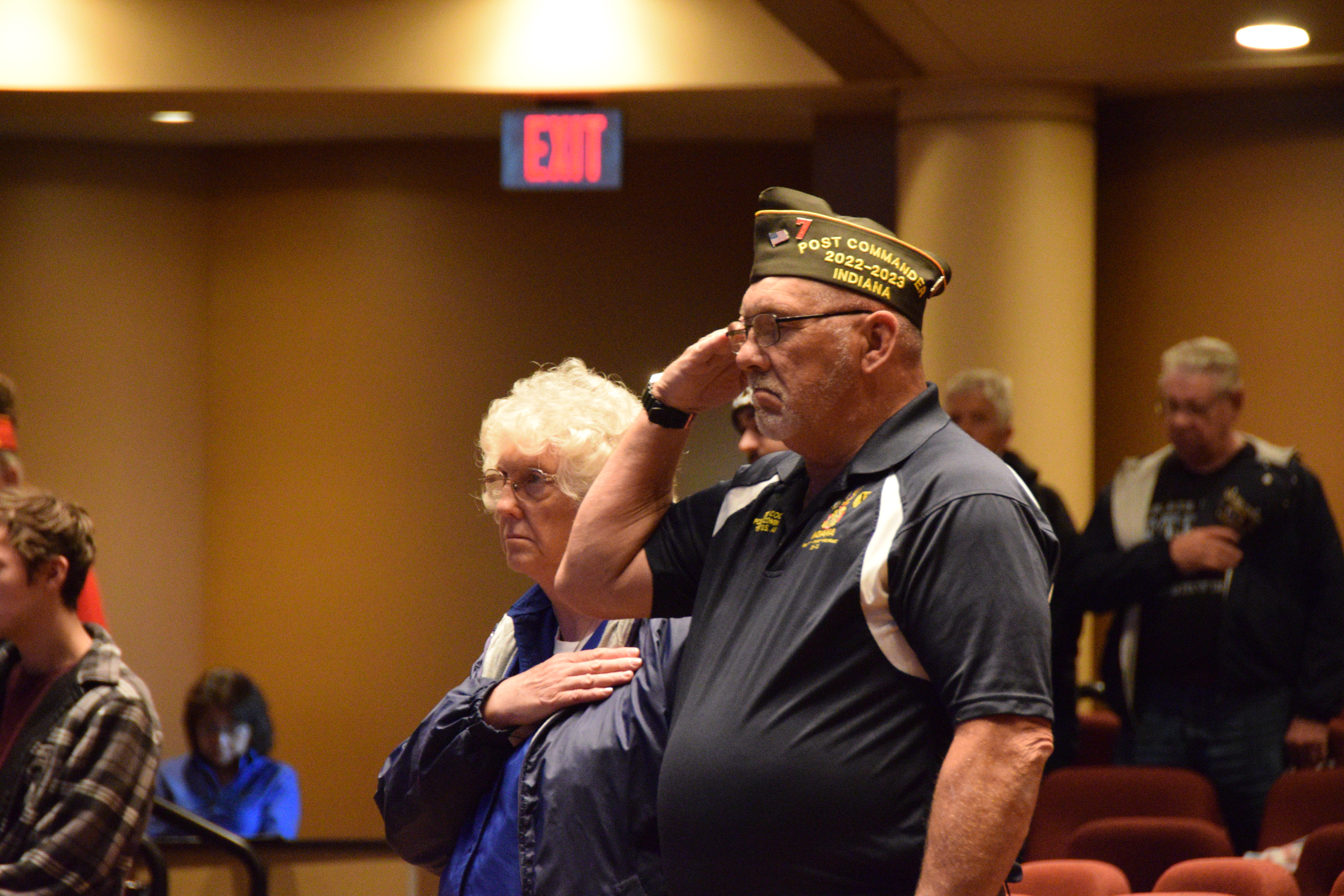 A male veteran salutes with a woman standing next to him.