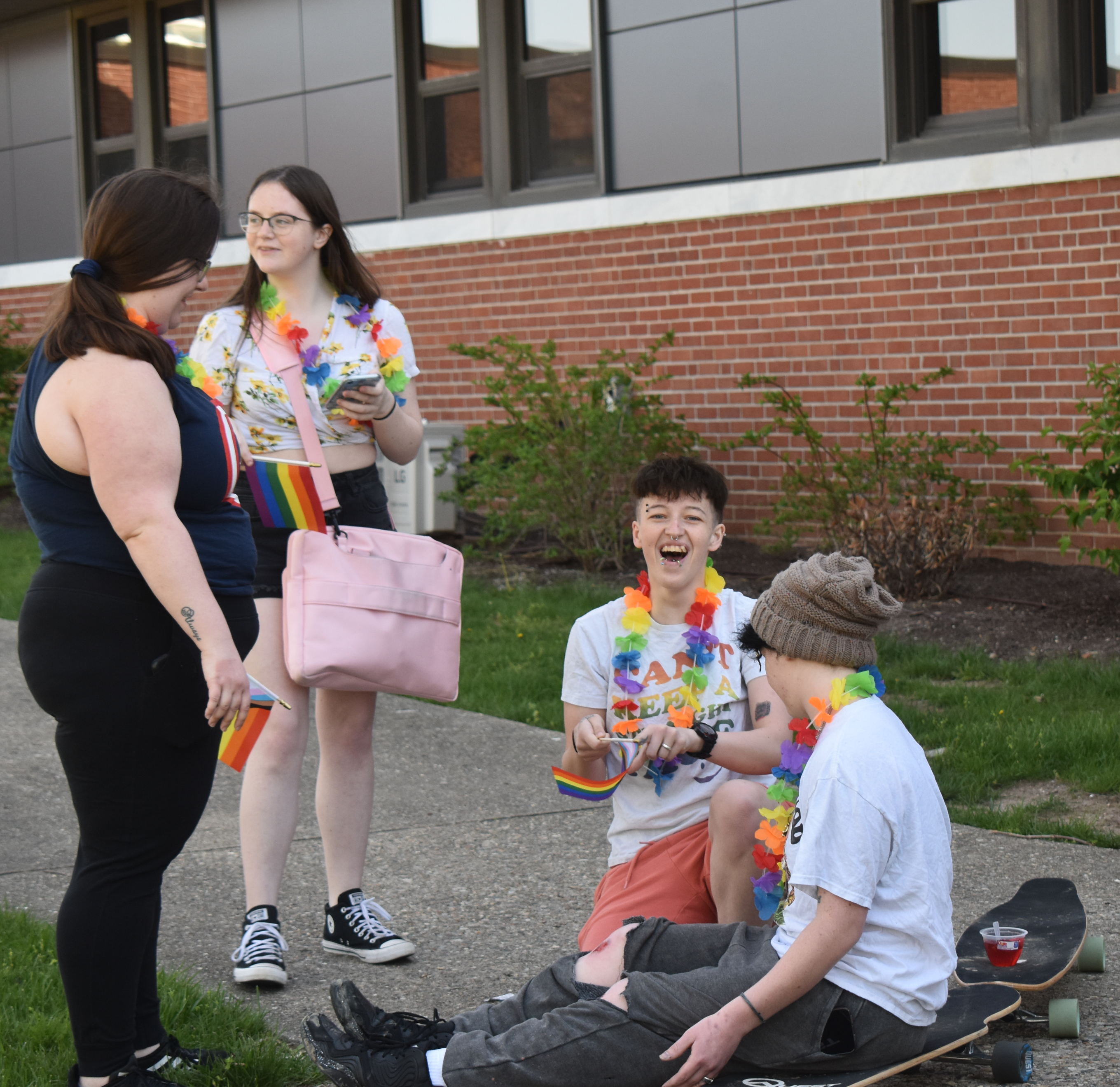Students standing near students sitting on a skateboarder while wearing rainbow-colored clothing and accessories